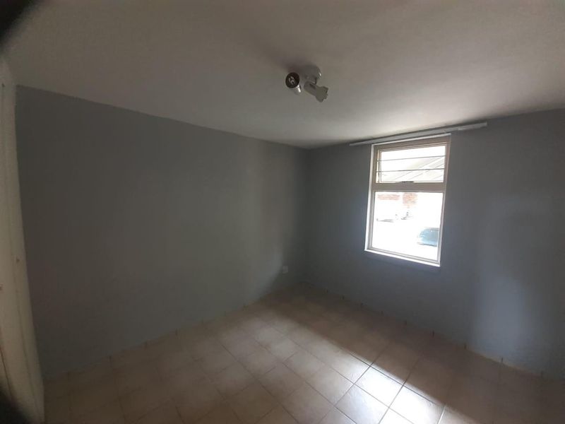 An empty bedroom featuring neutral grey walls, tiled flooring, and a window with security bars, providing a blank canvas for personalization.