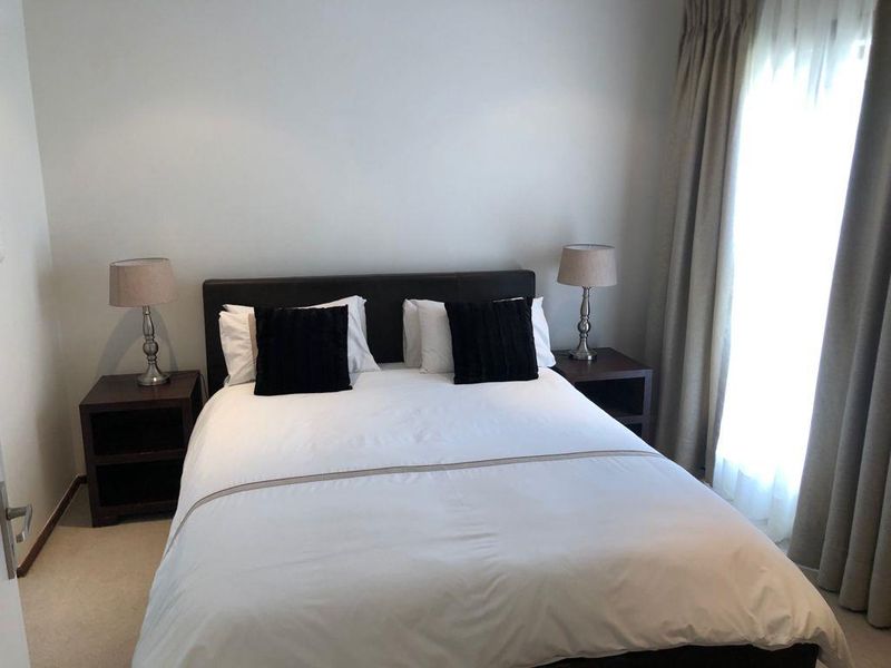 A well-maintained bedroom featuring neutral wall finishes, carpeted flooring, and floor-to-ceiling curtains providing natural light.