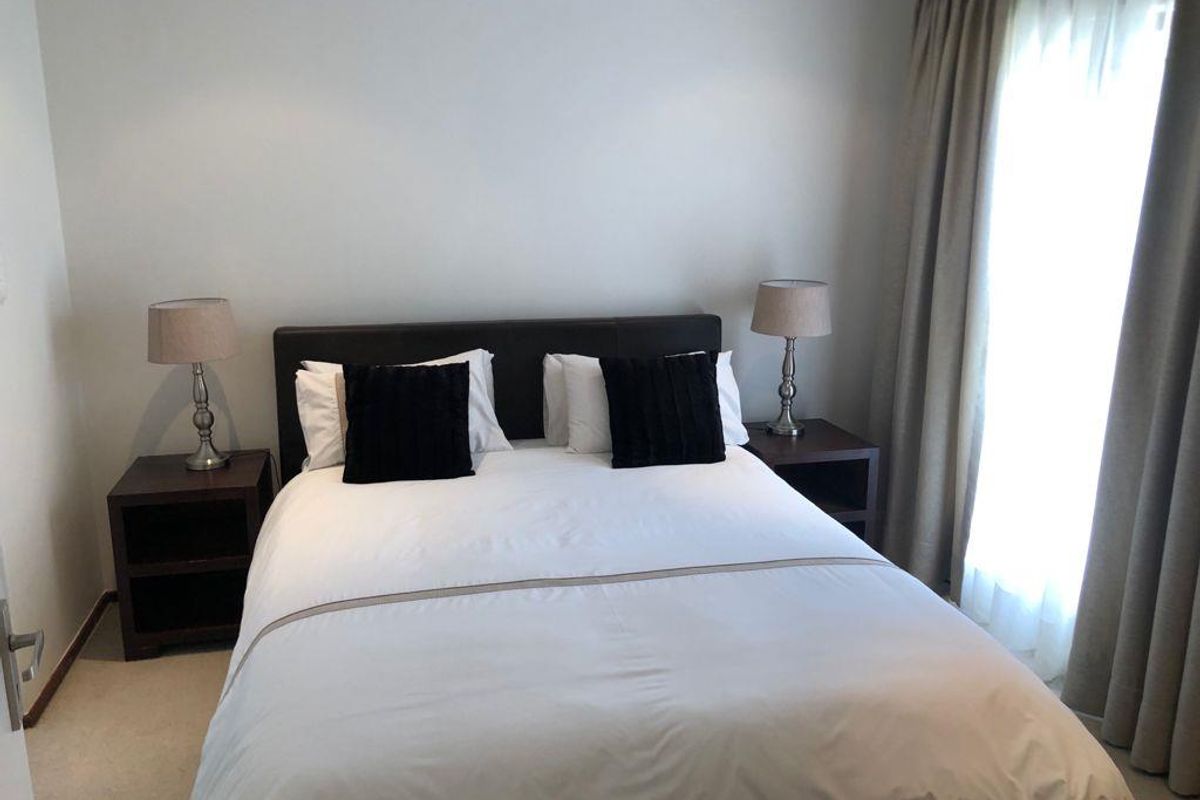 A well-maintained bedroom featuring neutral wall finishes, carpeted flooring, and floor-to-ceiling curtains providing natural light.