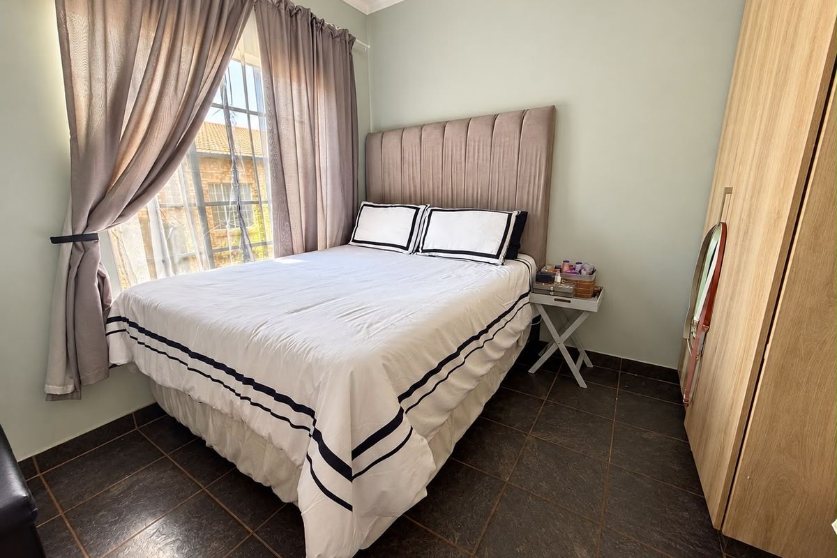 A cozy bedroom featuring tiled flooring, a built-in wardrobe, and a window with natural light.