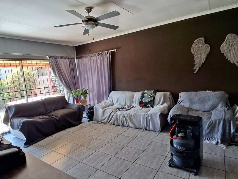 A living room featuring tiled flooring, a ceiling fan, and a sliding glass door with security gate access to the exterior.