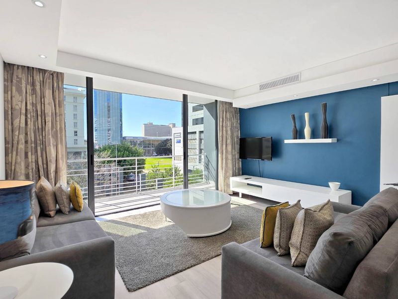 Modern living room featuring large sliding glass doors leading to a balcony, recessed lighting, ducted air conditioning, and contemporary blue accent wall.