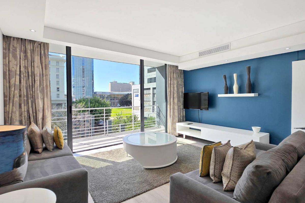 Modern living room featuring large sliding glass doors leading to a balcony, recessed lighting, ducted air conditioning, and contemporary blue accent wall.