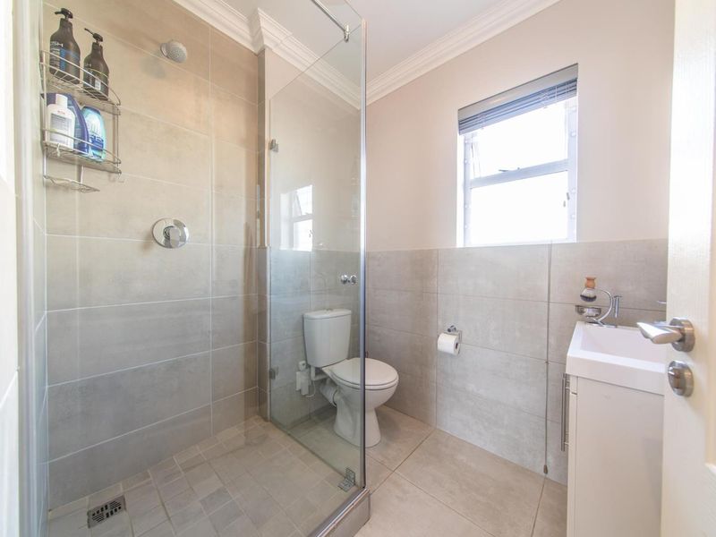Modern bathroom featuring a walk-in shower with glass screen, vanity basin, and neutral floor-to-ceiling tiling.