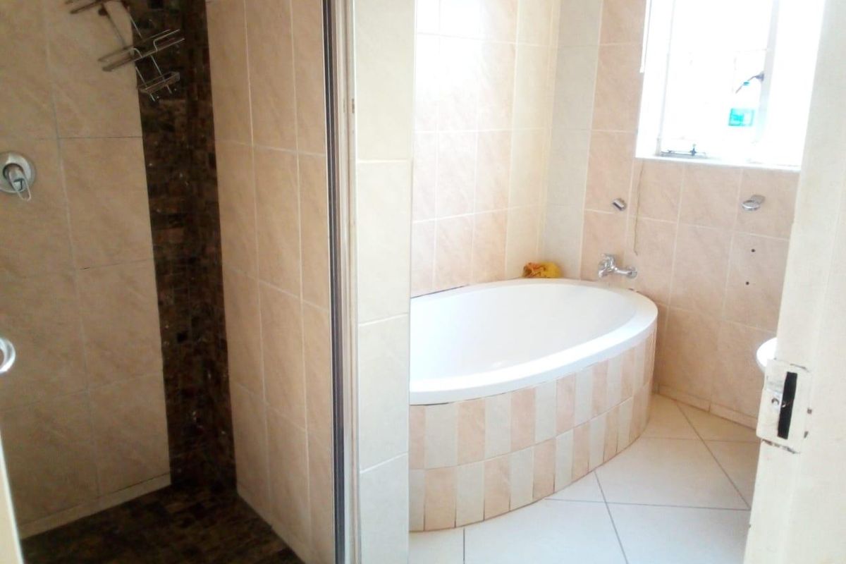 A functional bathroom featuring a built-in bathtub, separate shower enclosure, and neutral tiled finishes throughout.