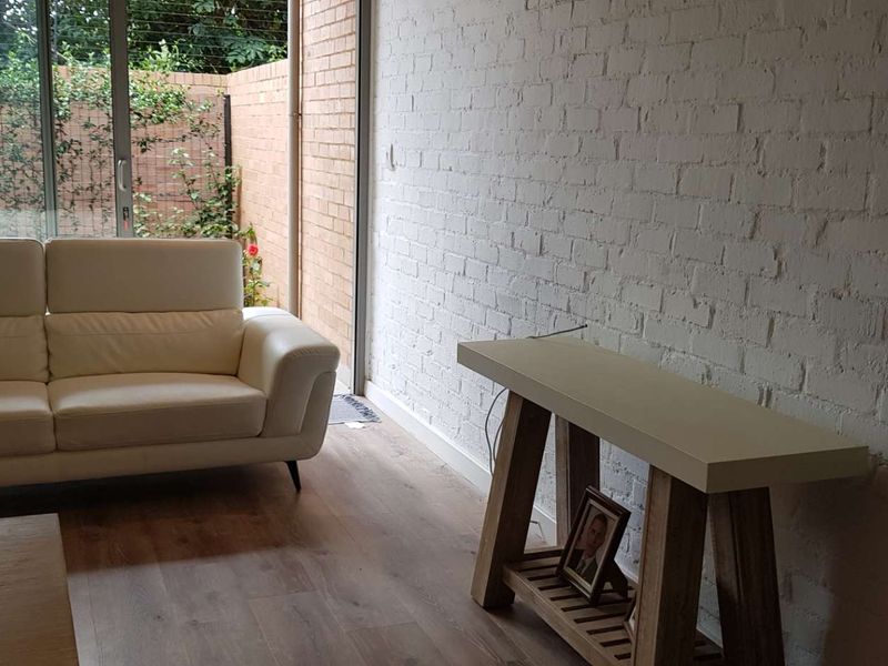 A bright living room featuring a painted exposed brick wall, modern laminate flooring, and large sliding glass doors opening to an outdoor area.