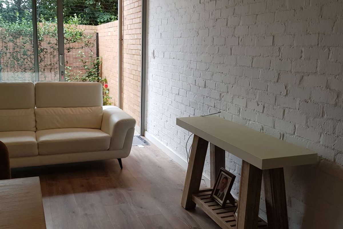 A bright living room featuring a painted exposed brick wall, modern laminate flooring, and large sliding glass doors opening to an outdoor area.