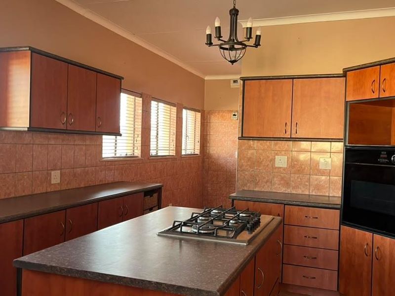 A spacious kitchen featuring wood-finish cabinetry, a central island with a gas cooktop, built-in oven, and tiled splashbacks.