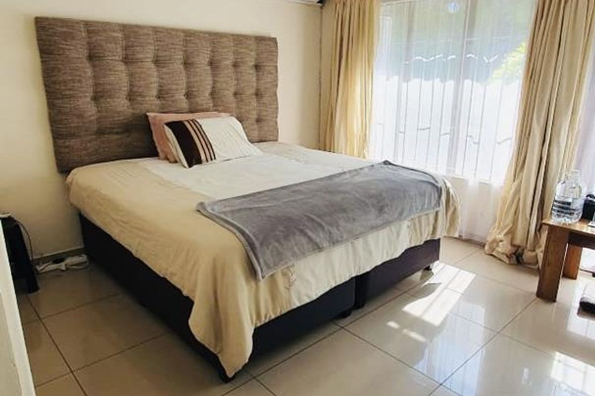 A well-lit bedroom featuring large format floor tiles, a wall-mounted air conditioning unit, and a large window with natural light.