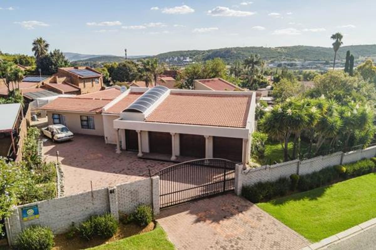 Aerial view of a residential property featuring a triple garage, tiled roof with a skylight, paved driveway, and perimeter walling with a gated entrance.