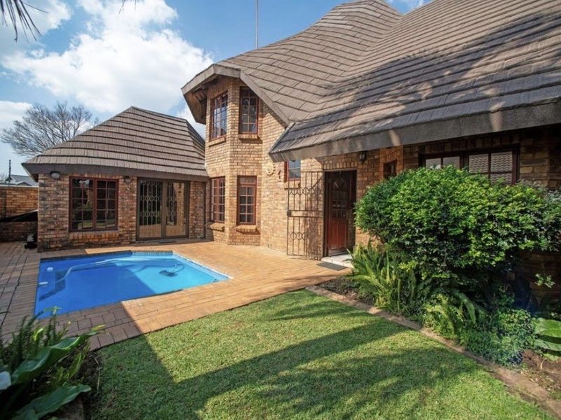 Rear exterior view of a face-brick cluster home featuring a private swimming pool, paved patio area, and established garden.
