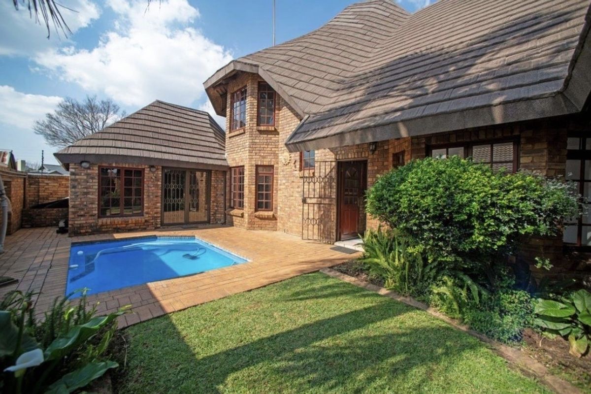 Rear exterior view of a face-brick cluster home featuring a private swimming pool, paved patio area, and established garden.