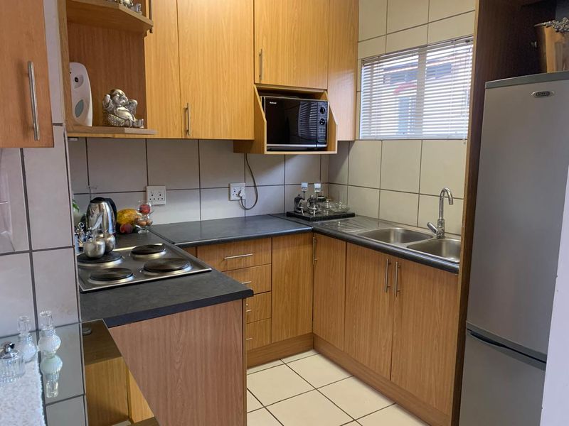 Compact kitchen featuring laminate cabinetry, dark countertops, built-in electric hob, and stainless steel sink with tiled splashbacks and flooring.