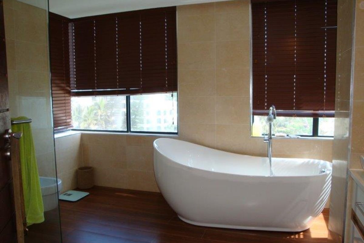 Modern bathroom featuring a freestanding white bathtub, large format wall tiles, dark wood-look flooring, and timber venetian blinds.