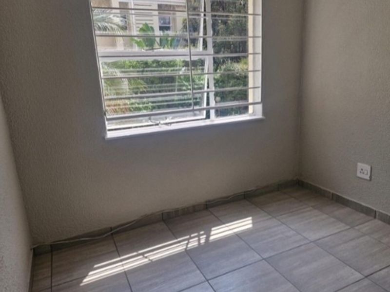 An empty bedroom featuring neutral tiled flooring, textured walls, and a window fitted with security bars.