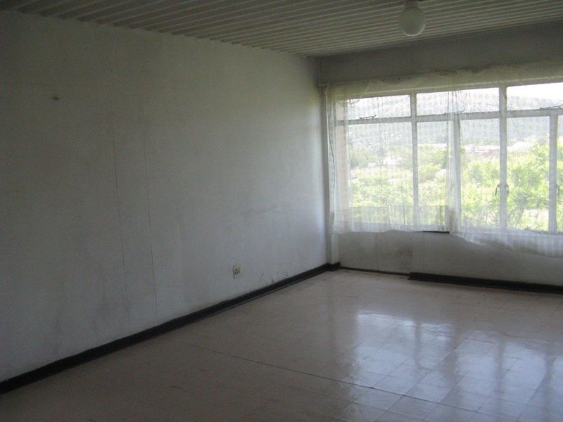 An empty, sunlit living area featuring large windows, tiled flooring, and neutral walls, offering a blank canvas for renovation and interior design.