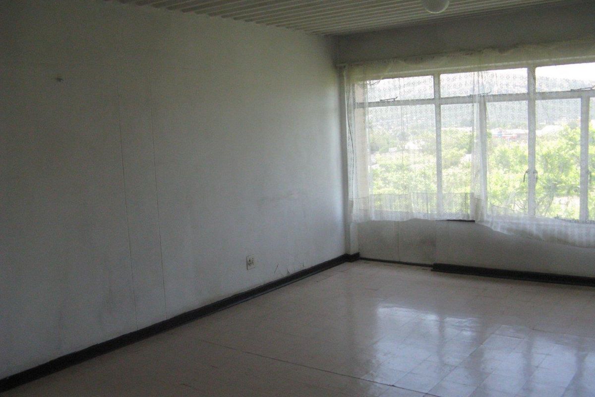 An empty, sunlit living area featuring large windows, tiled flooring, and neutral walls, offering a blank canvas for renovation and interior design.