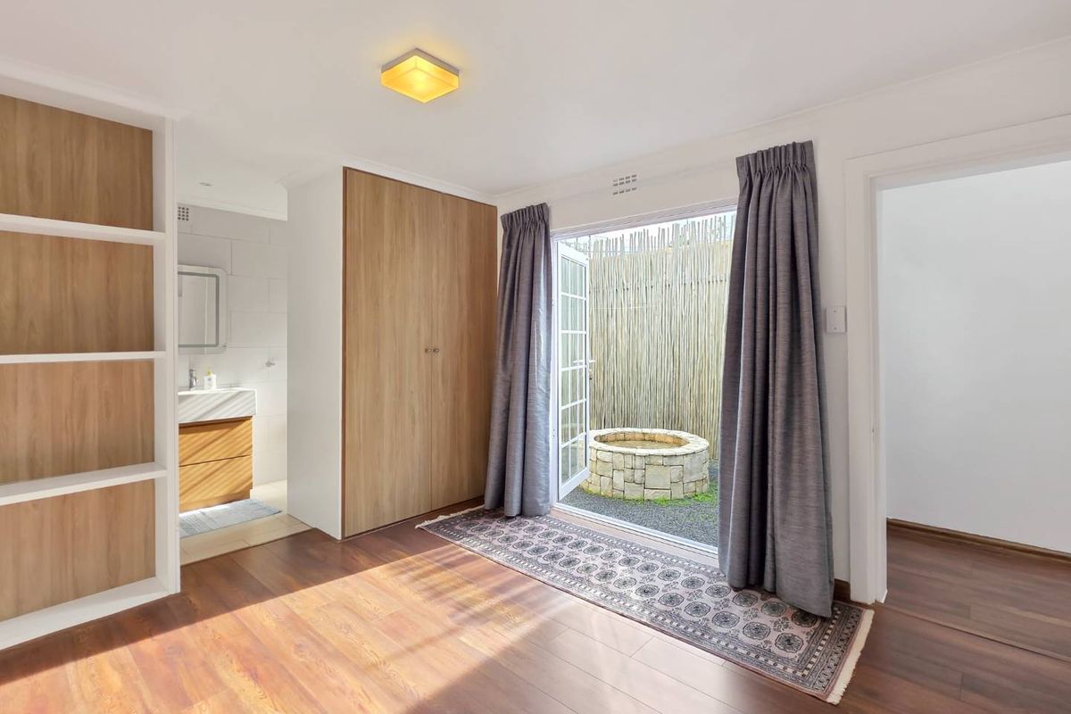 Bright bedroom featuring laminate flooring, built-in cupboards, and direct access to a private courtyard area with an en-suite bathroom.