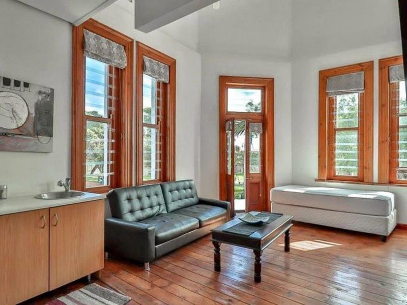 A bright living area featuring warm timber flooring, natural wood window frames, and a convenient built-in kitchenette with a sink.
