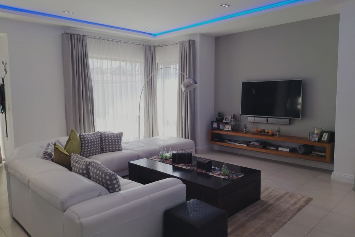 Modern living room featuring recessed ceiling lighting with blue LED accents, tiled flooring, and a custom wall-mounted timber media console.