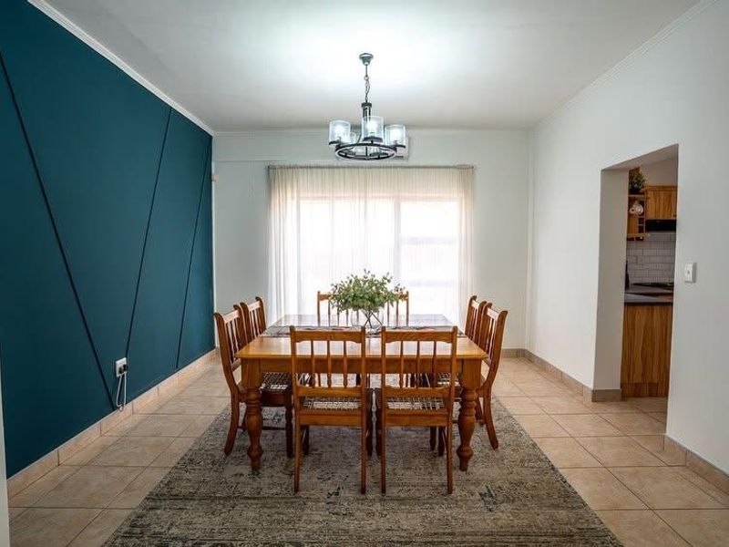 A well-maintained dining room featuring tiled flooring, a striking teal accent wall, and a central light fixture, with an adjacent view into the kitchen.