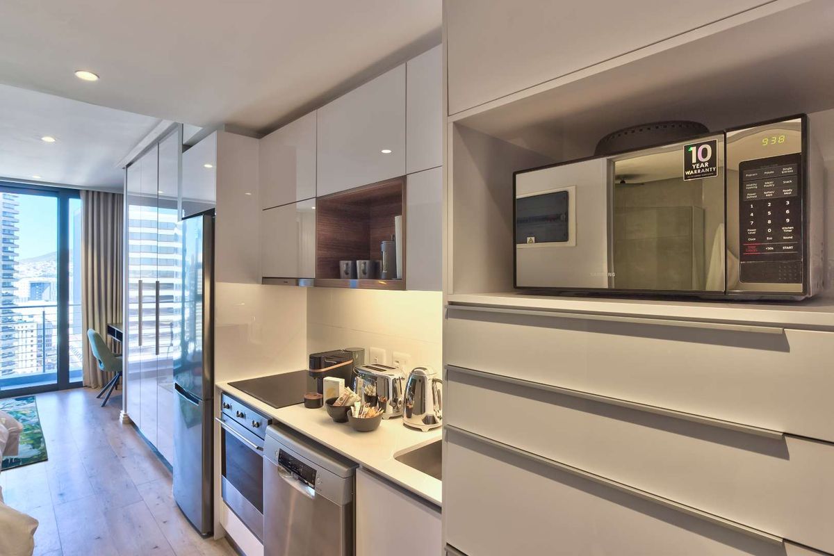 Modern compact kitchen featuring high-gloss cabinetry, stone countertops, integrated appliances, and recessed lighting, seamlessly flowing into the adjacent living area.