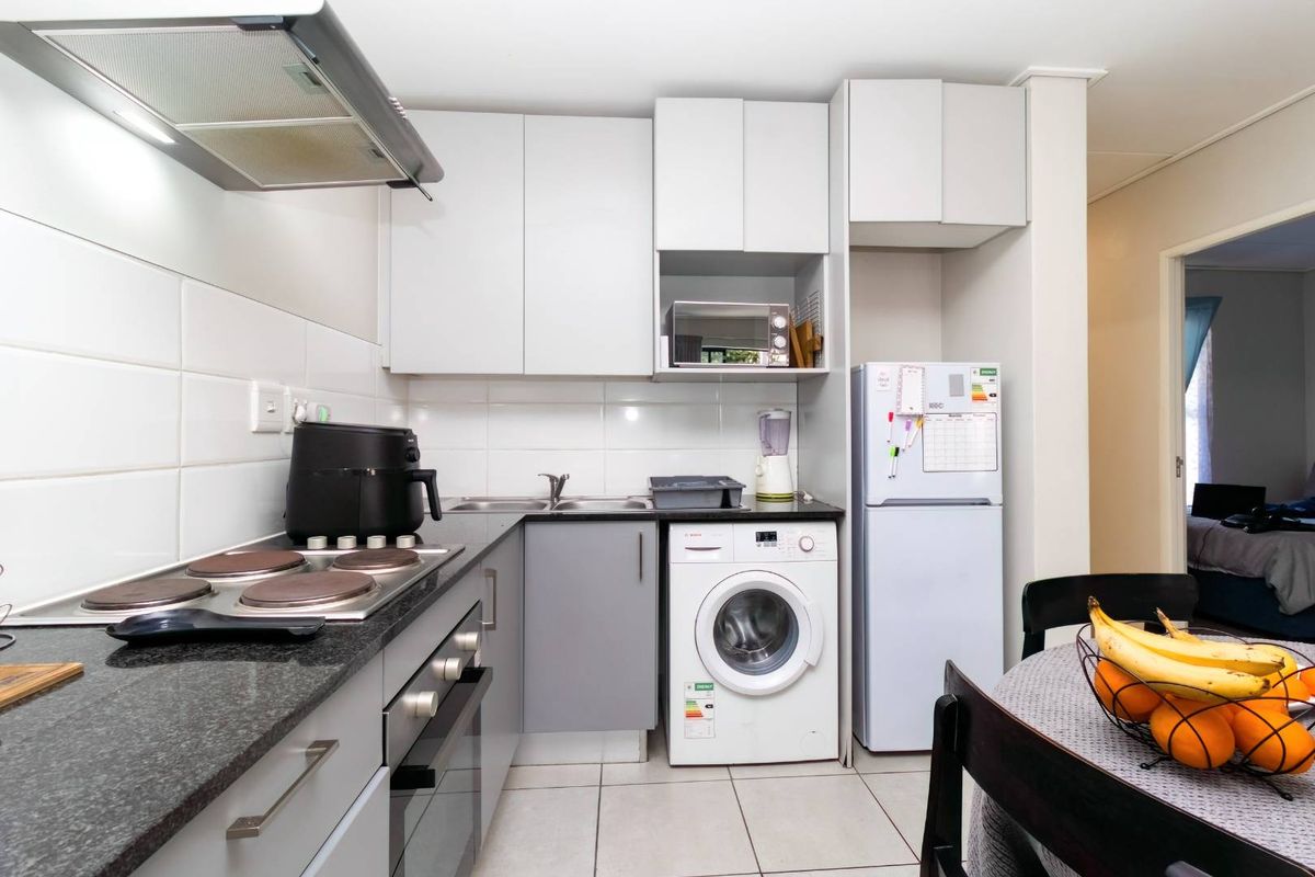 Compact kitchen featuring grey cabinetry, dark granite countertops, integrated electric hob, oven, extractor fan, and space for a washing machine.