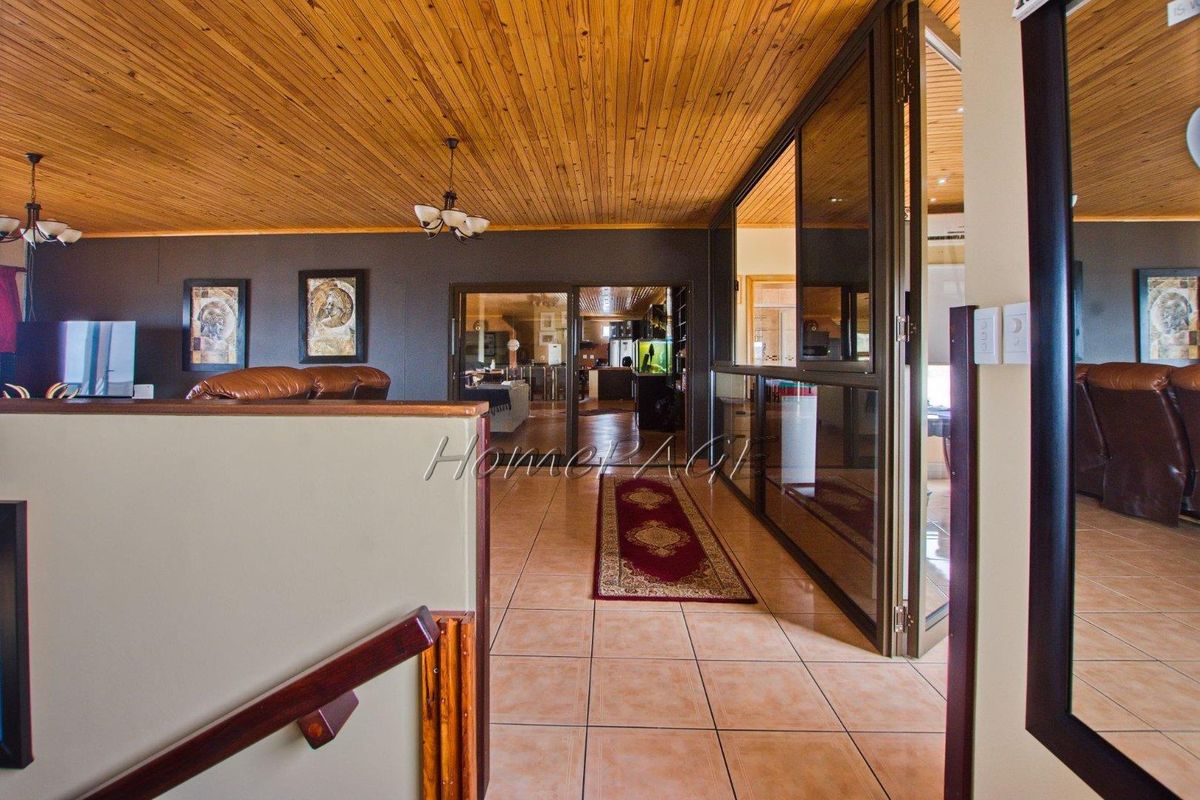 Spacious living area featuring a timber-clad ceiling, tiled flooring, and glass-panelled room dividers leading to adjacent living spaces.