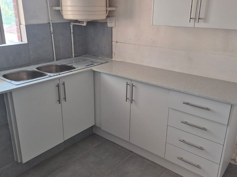 A functional kitchen area featuring white cabinetry, laminate countertops, and a double sink, currently requiring finishing touches to the walls and plumbing.