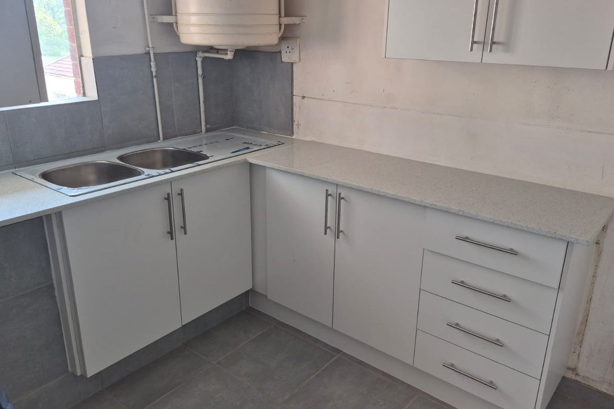 A functional kitchen area featuring white cabinetry, laminate countertops, and a double sink, currently requiring finishing touches to the walls and plumbing.