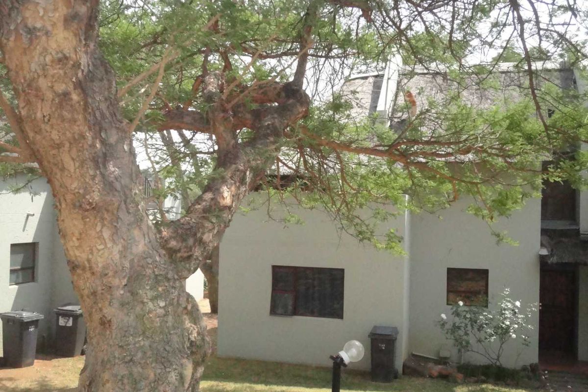 Exterior view of the apartment building featuring a neutral facade, mature trees, and surrounding garden area.