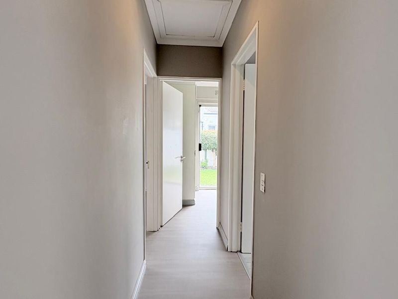 A clean, neutral-toned hallway featuring white architraves, skirting boards, and a ceiling access hatch, leading towards an exterior doorway.