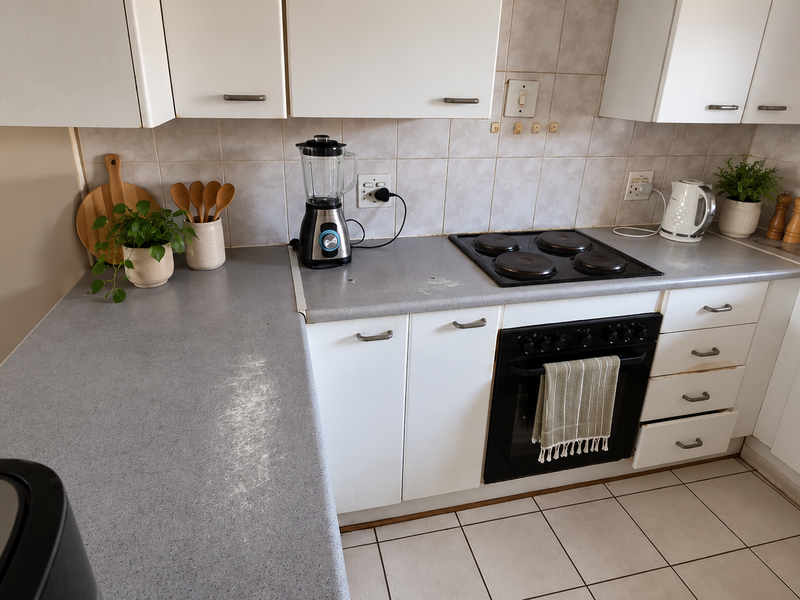 A functional kitchen featuring laminate countertops, built-in oven, electric hob, tiled backsplash, and ample white cabinetry with ceramic floor tiles.