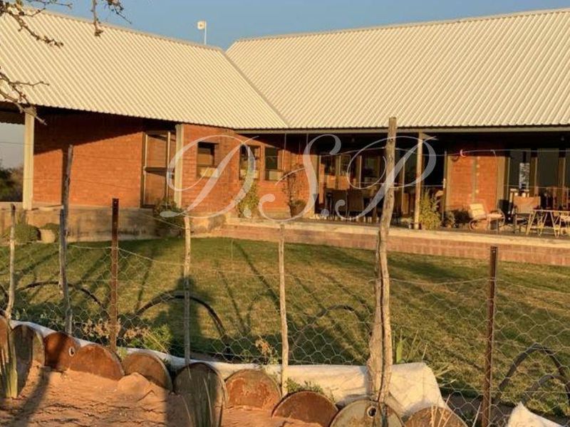 Rear view of a farm-style residence featuring exposed brick walls, a corrugated metal roof, and a covered patio overlooking a lawn area.