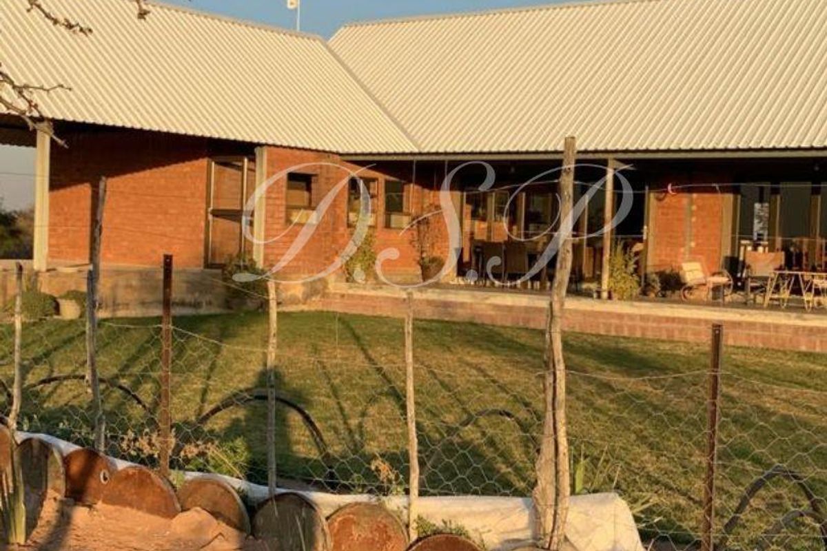 Rear view of a farm-style residence featuring exposed brick walls, a corrugated metal roof, and a covered patio overlooking a lawn area.