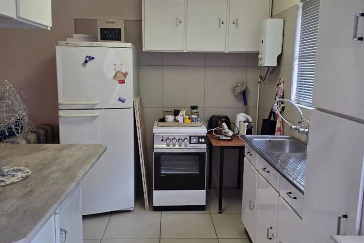 A functional kitchen featuring white cabinetry, tiled flooring, a stainless steel sink, and a freestanding stove, offering potential for modern updates.