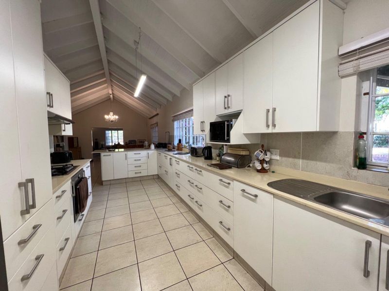 Spacious kitchen featuring white cabinetry, stone countertops, built-in appliances, and a high vaulted ceiling with tiled flooring.