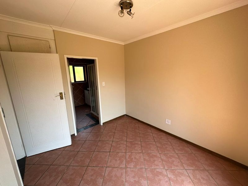 An empty bedroom featuring tiled flooring and neutral walls, with an adjoining bathroom visible through the doorway.
