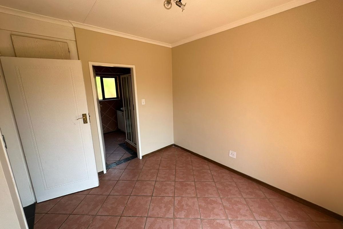 An empty bedroom featuring tiled flooring and neutral walls, with an adjoining bathroom visible through the doorway.