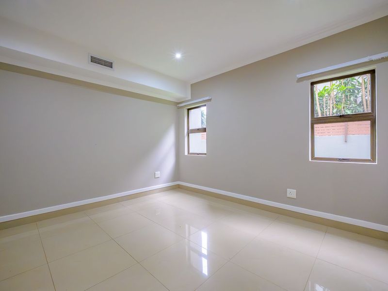 A bright, empty bedroom featuring neutral wall tones, polished tiled flooring, recessed lighting, and an integrated air conditioning vent.