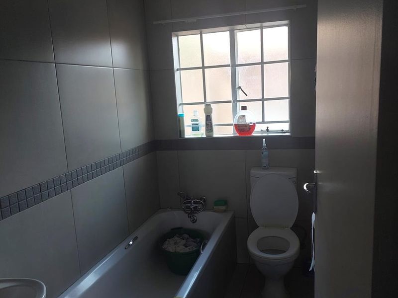 A functional bathroom featuring a bathtub, toilet, and basin with neutral wall tiling and a window for natural light.