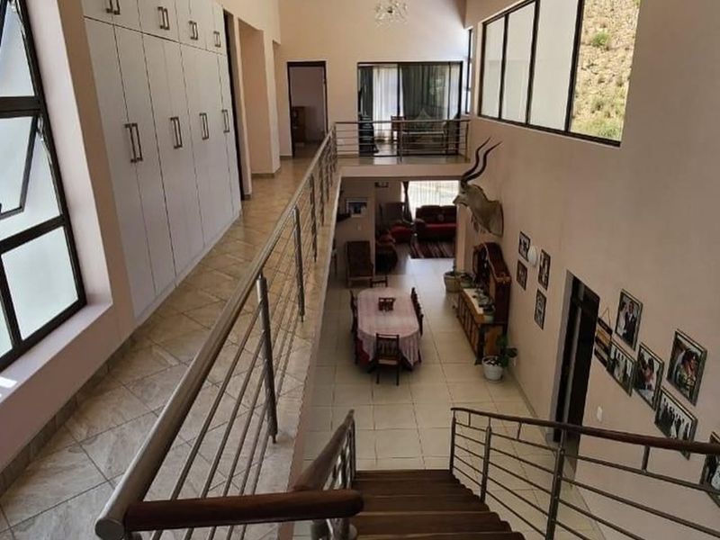 Spacious upper-level hallway featuring built-in cabinetry, tiled flooring, and a modern stainless steel balustrade overlooking the dining area below.