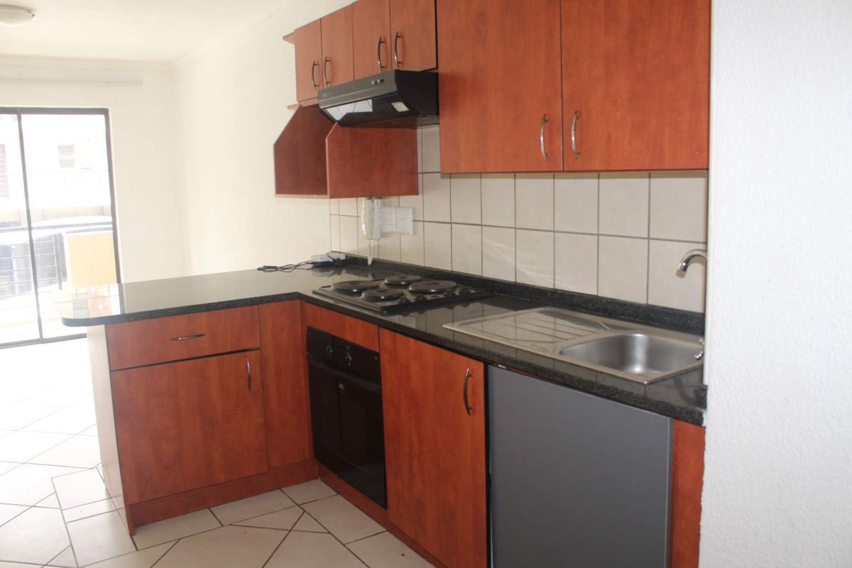 A functional kitchen featuring wood-look cabinetry, granite countertops, built-in oven, hob, and extractor fan, with tiled flooring and backsplash.