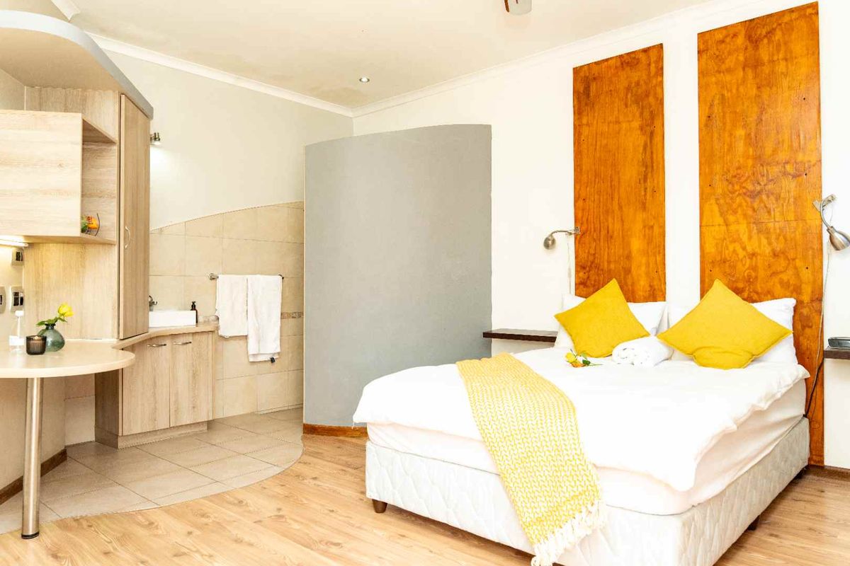 A hotel bedroom featuring laminate flooring, a built-in vanity area, and decorative wooden wall panels behind the bed.