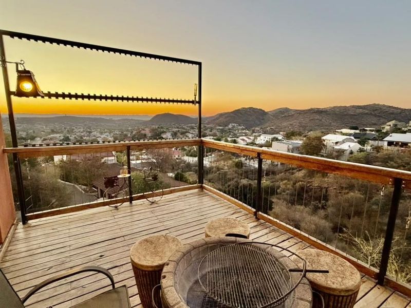 Elevated balcony featuring timber decking, steel cable balustrades, and a built-in fire pit, offering expansive panoramic mountain and valley views.