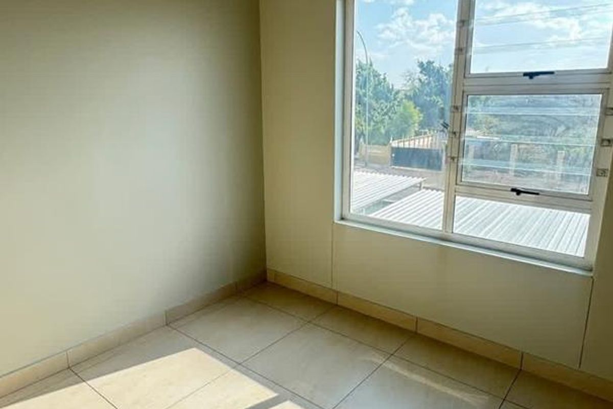 A bright, empty bedroom featuring large tiled flooring, neutral wall tones, and a window with security bars providing natural light.