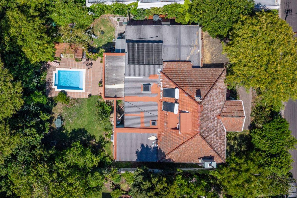 Aerial view of the property showing the main house structure, tiled roof, solar panels, swimming pool, and surrounding garden area.
