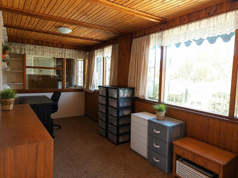 A home office space featuring extensive timber-clad walls and ceilings, large windows providing natural light, and carpeted flooring.