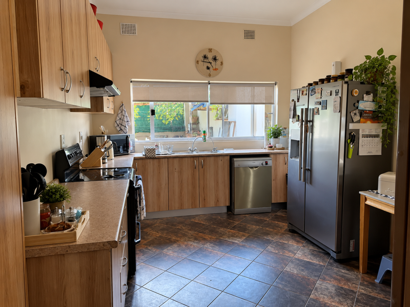 A functional kitchen featuring light wood-look cabinetry, laminate countertops, tiled flooring, and integrated appliances including a hob, oven, and extractor fan.