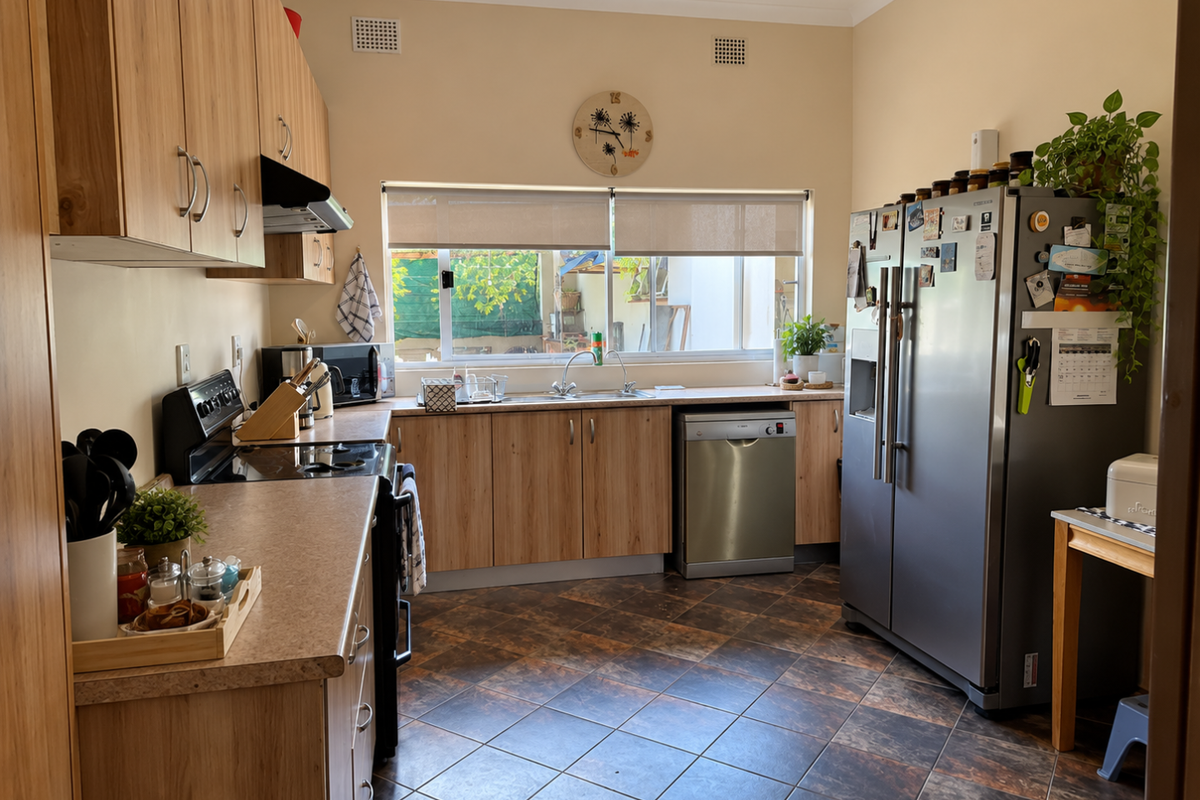 A functional kitchen featuring light wood-look cabinetry, laminate countertops, tiled flooring, and integrated appliances including a hob, oven, and extractor fan.